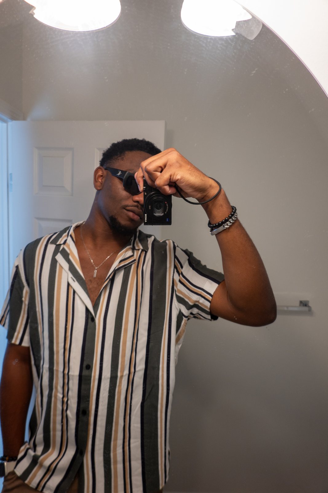 Chiemeka Madufor taking a mirror photo with a compact camera, in a striped shirt