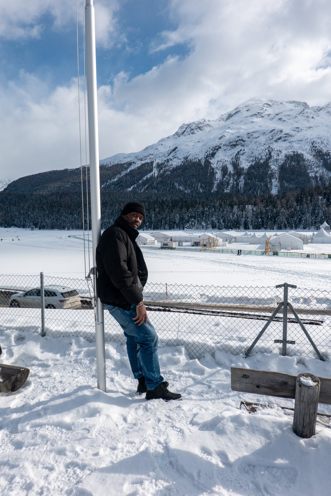Chiemeka Madufor leaning on a pole in the snow, with mountains behind